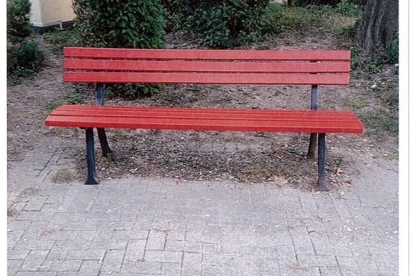 Rote Ruhebank, dahinter Hecken und ein Baum