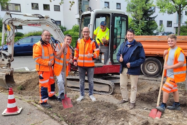 Sechs Männer auf einer Baustelle. Einer der Männer sitzt in einem Bagger