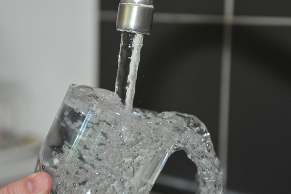 Aus dem Wasserhahn fließt Wasser in ein Glas